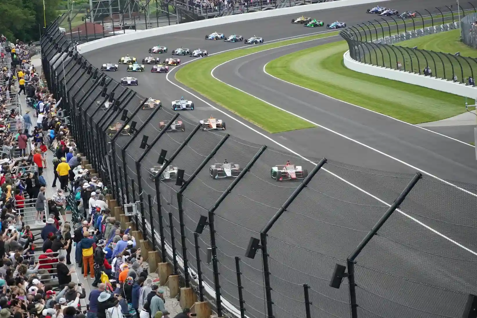 Monoplaces en course sur l'ovale de l'Indianapolis Motor Speedway devant des tribunes pleines de spectateurs.